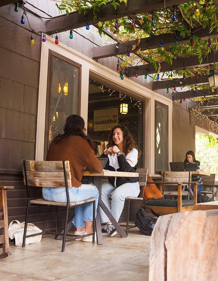 two students visit at a cafe tabel on the porch of the grove house